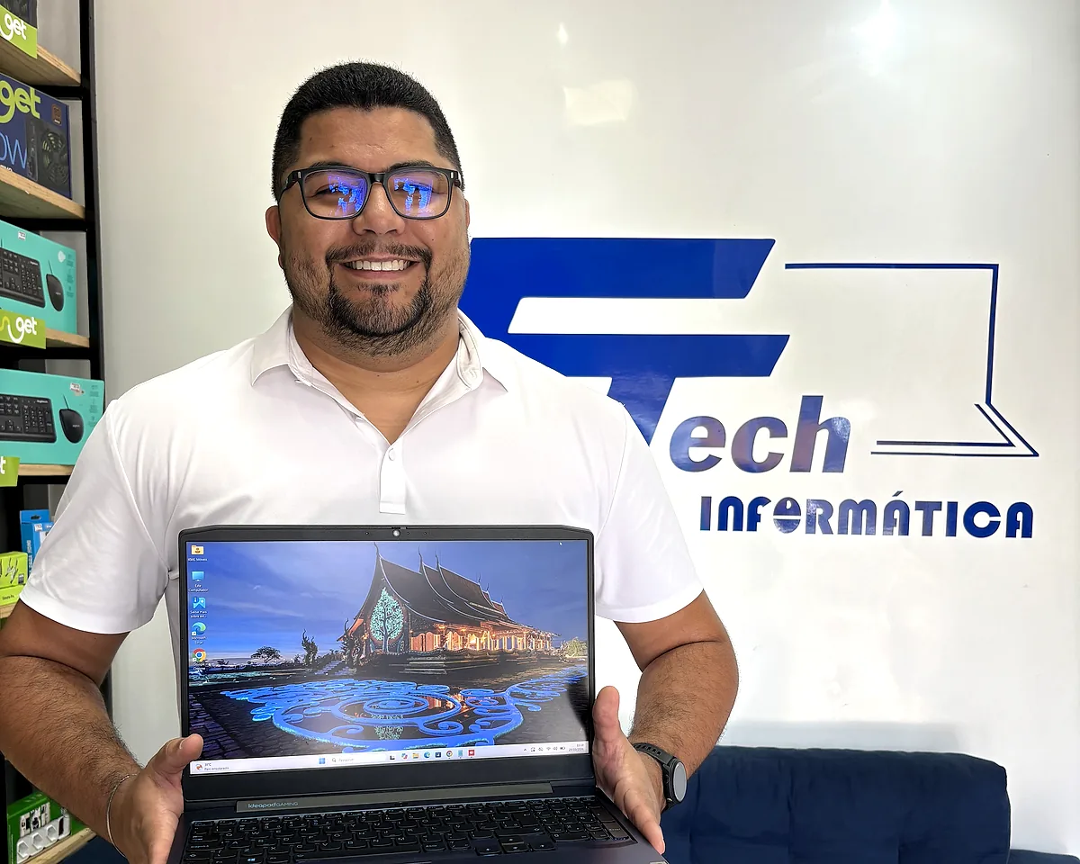 Especialista da FTech segurando um notebook na loja, com o logo da FTech na parede